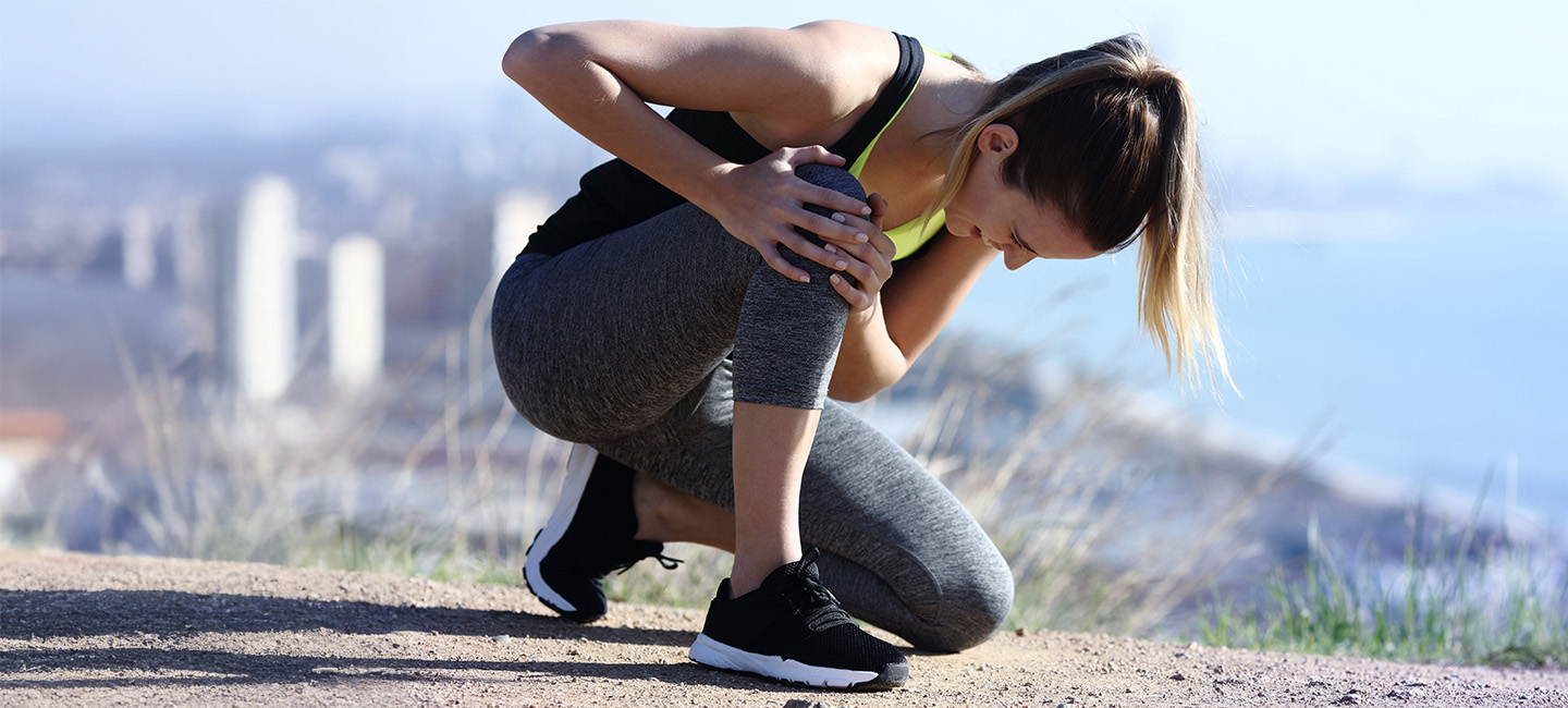 Frau sitzt auf der Couch mit Handy - am Bein ist eine Orthese